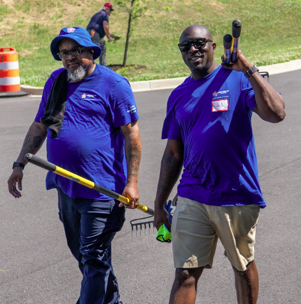 Two volunteers carrying rakes and tools during a corporate service day