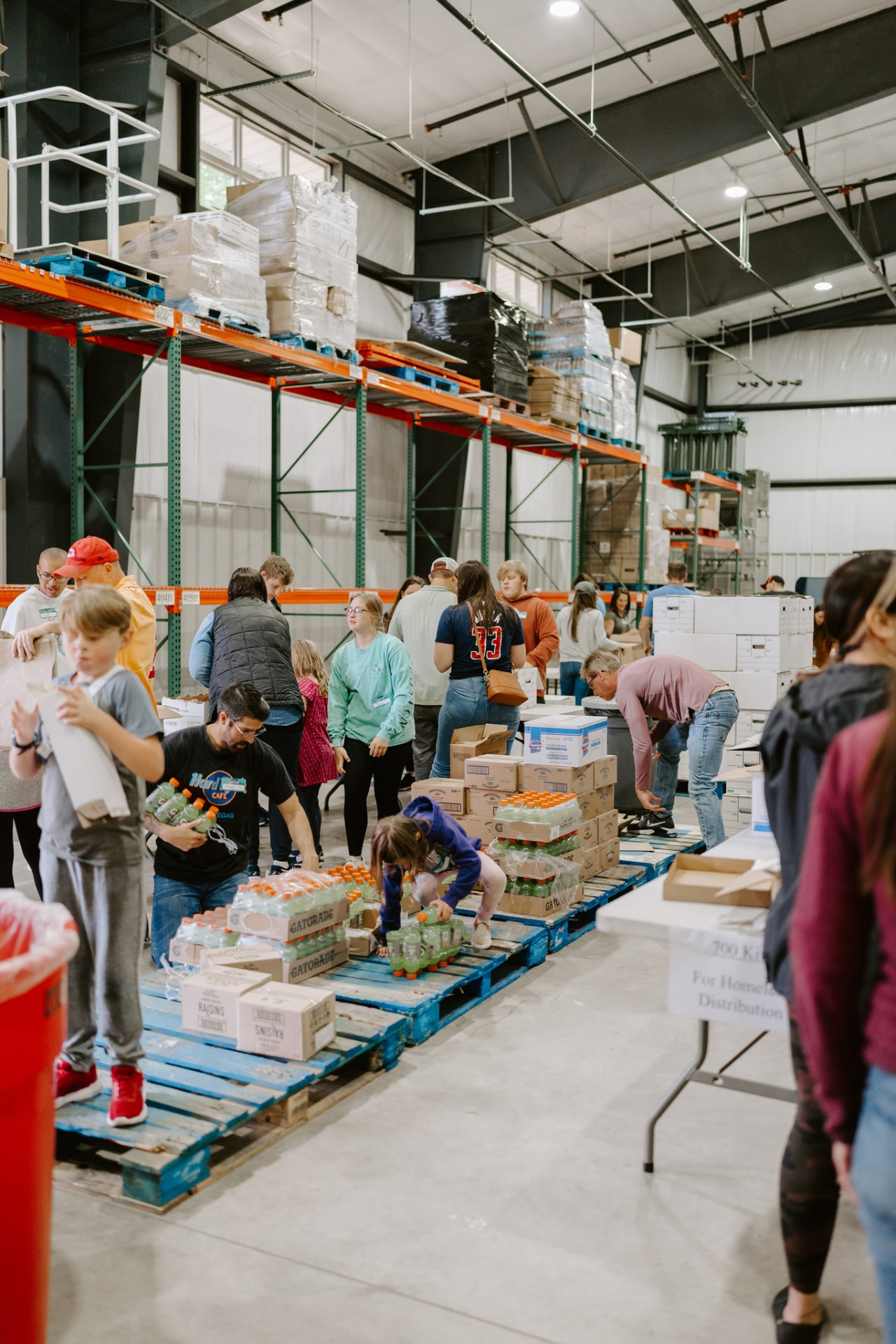 Volunteers of all ages sorting food and drinks on pallets in the Community Harvest Network warehouse